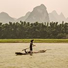 437 - Yangshuo - Fisherman on Bamboo Raft with his Cormorant. On Background the Karst Peaks