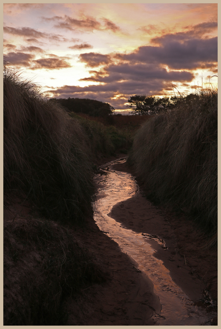 a stream through the dunes at embleton at dusk