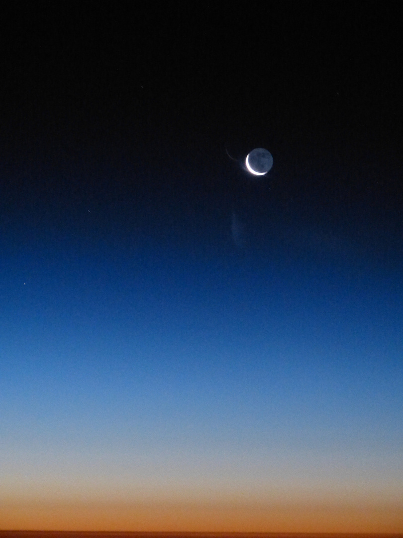 abnehmender Mond hoch über den Wolken beim ersten Morgenrot