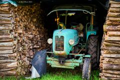 Alter Traktor versteckt in Holzstapeln am Mühlenwanderweg