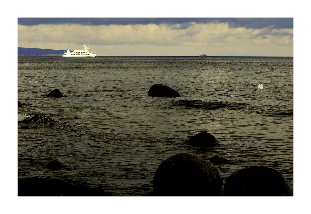 Am grauen Strand am grauen Meer und weitab fährt ein Schiff