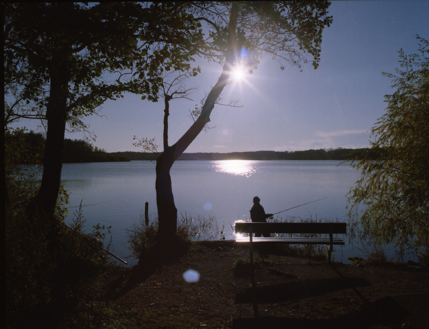 Angler und Bank im Gegenlicht an den Krickenbecker Seen