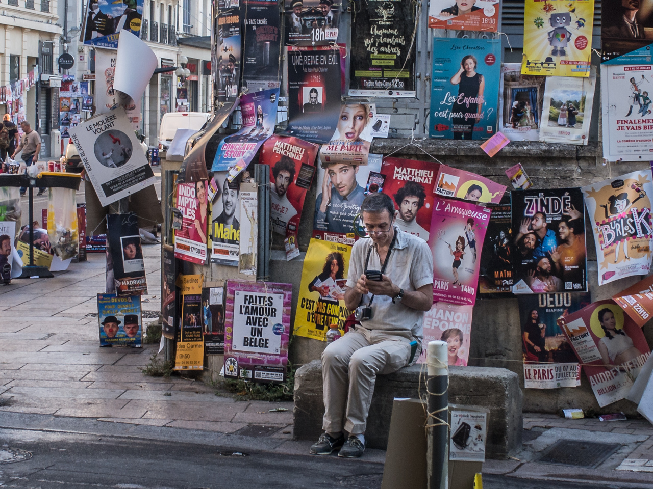 assis sur un banc en pierre, dos au mur, les yeux sur un écran, l'homme portait des chaussettes