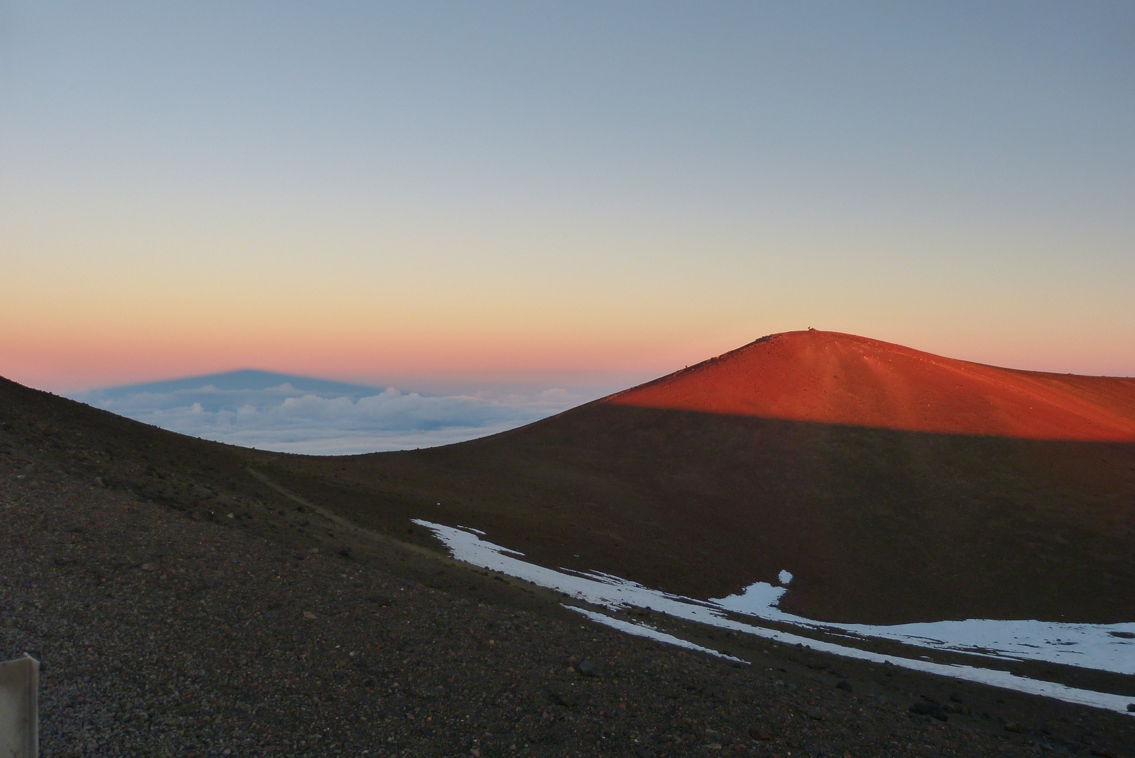 Auf 4205 Metern, wirft die untergehende Sonne des Schatten des Mauna Kea auf die Wolken.