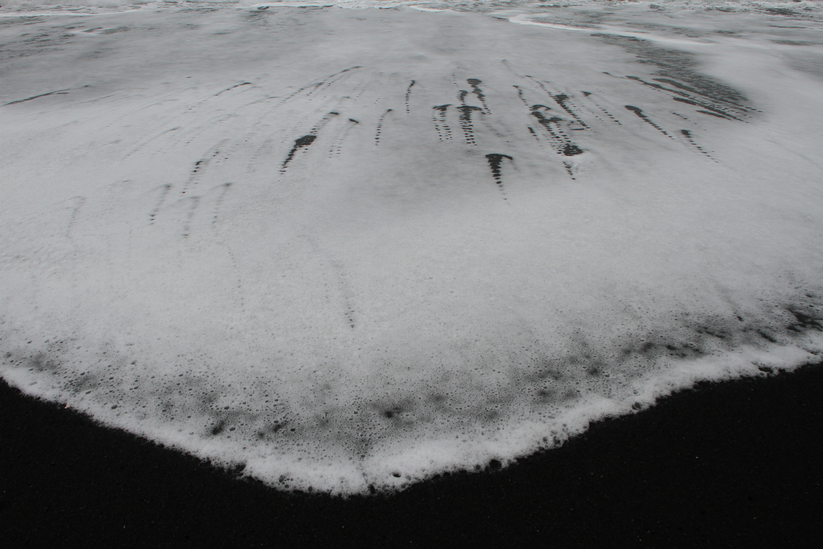 Auslaufende Welle auf schwarzem Sand