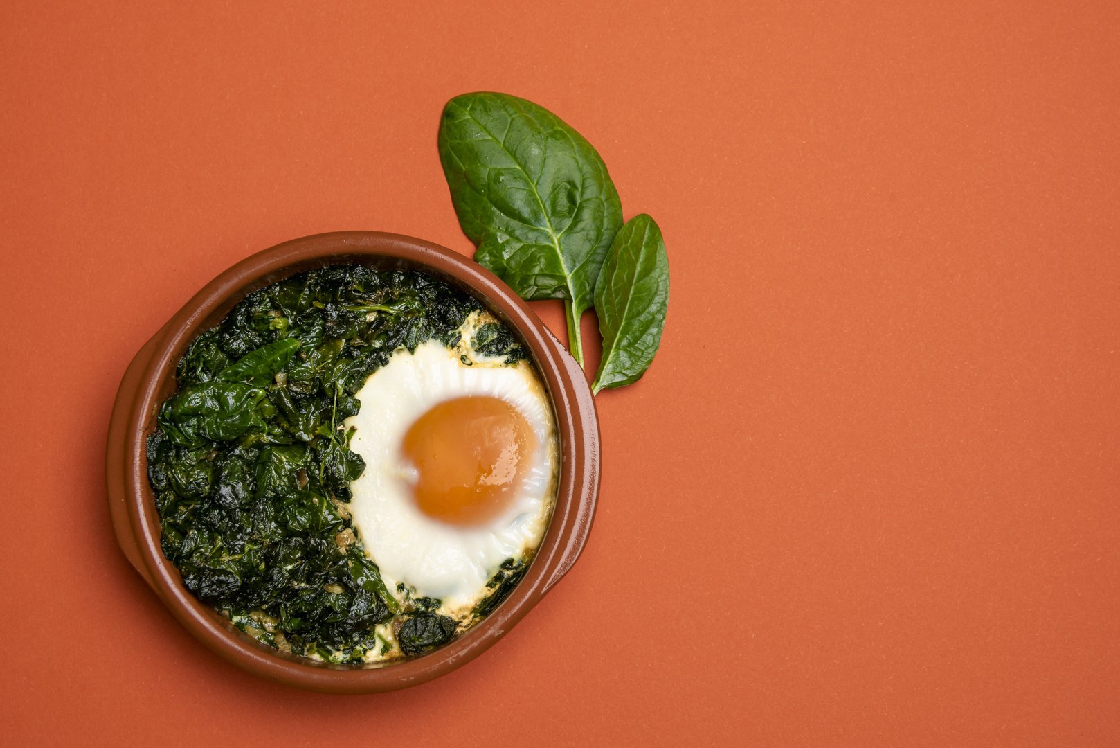 Baked spinach and egg in a clay pot. Flat lay image