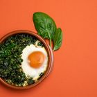 Baked spinach and egg in a clay pot. Flat lay image