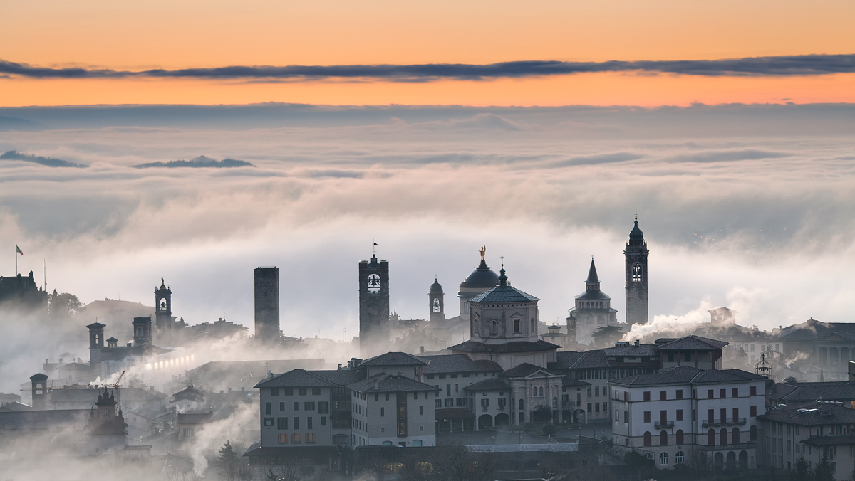 Bergamo Alta emerge sopra un mare di nuvole.