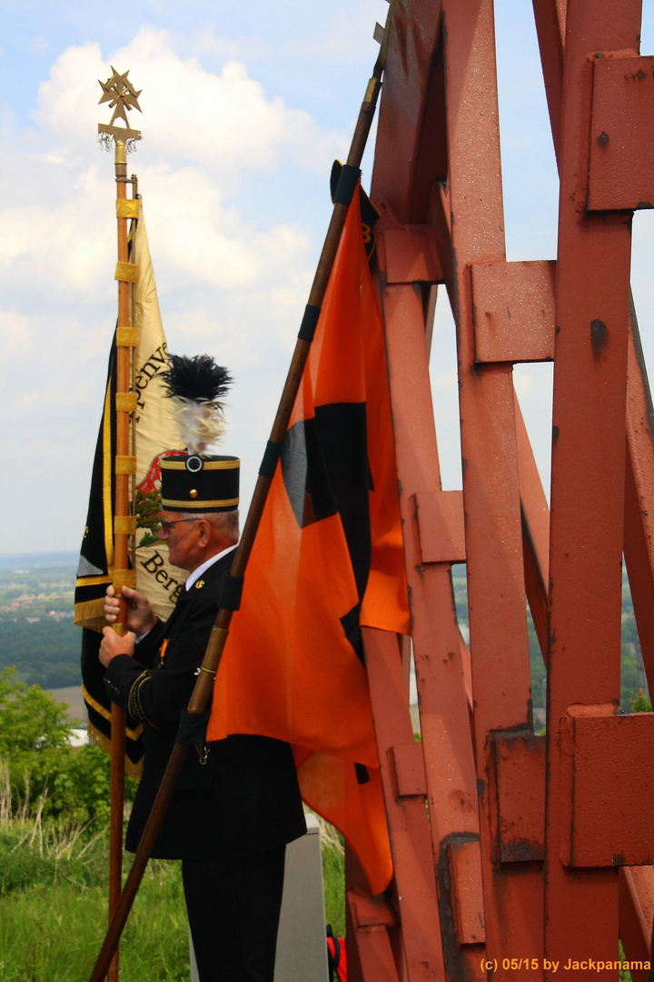 Bergmann neben einem halben Förderrad und dem Gipfelkreuz