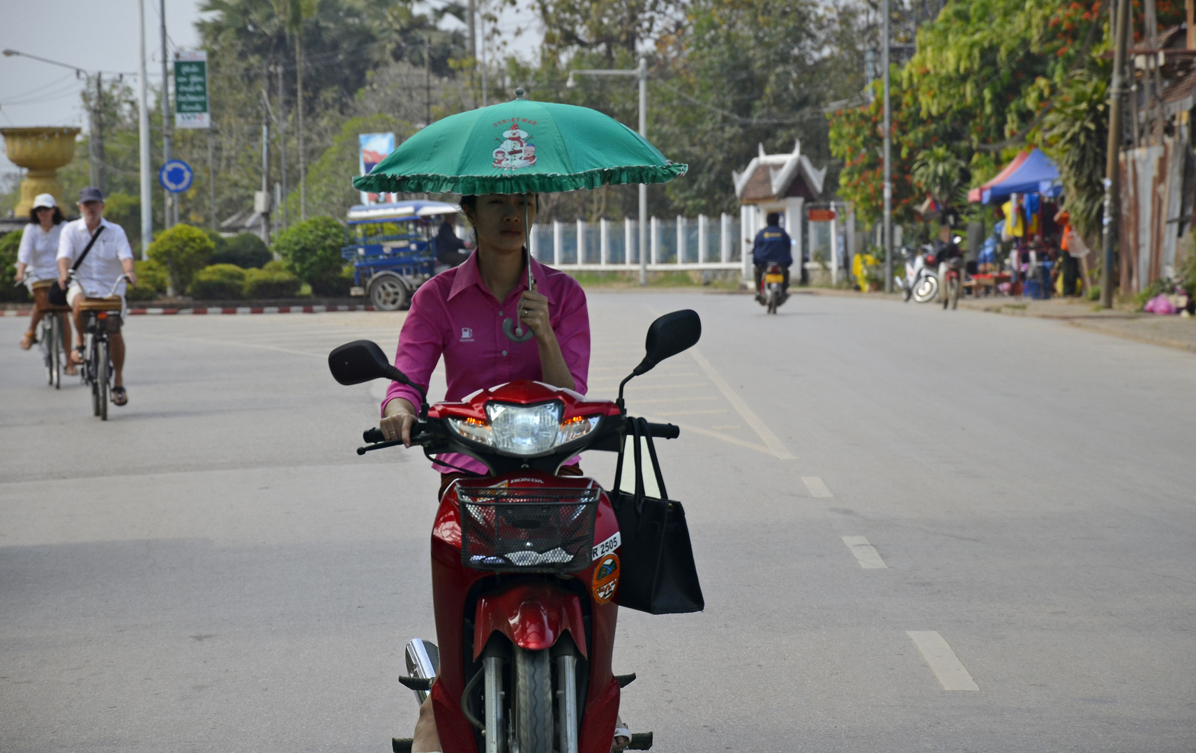 Beschirmte Zweirad-Fahrerin in Laos.
