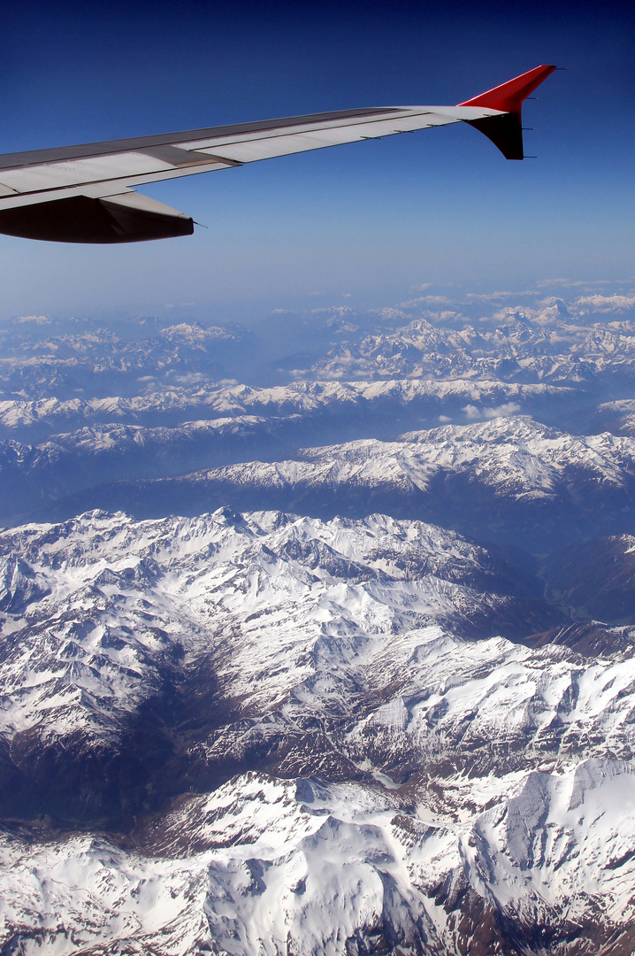 Blick aus dem Flugzeugfenster auf die vom Schnee bedeckten österreichischen Alpen