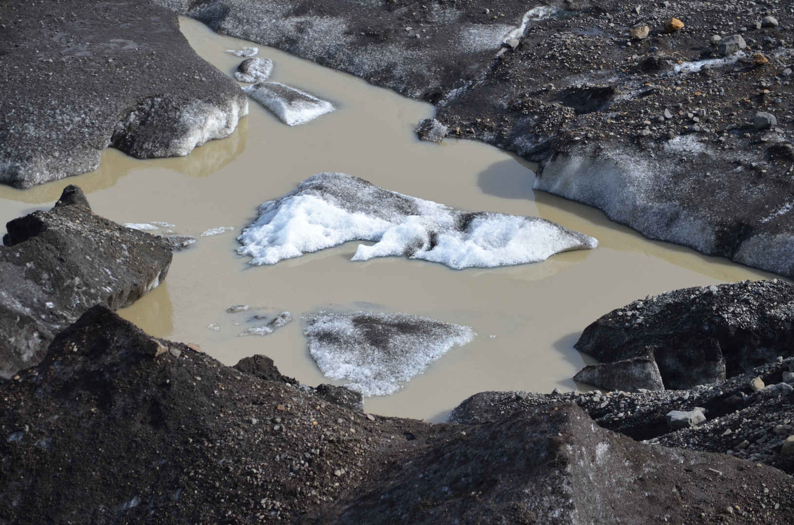 Braungelbmilchiges Wasser und schwarzes Eis in einer Gletscherlagune eines Vatnökökullausläufers