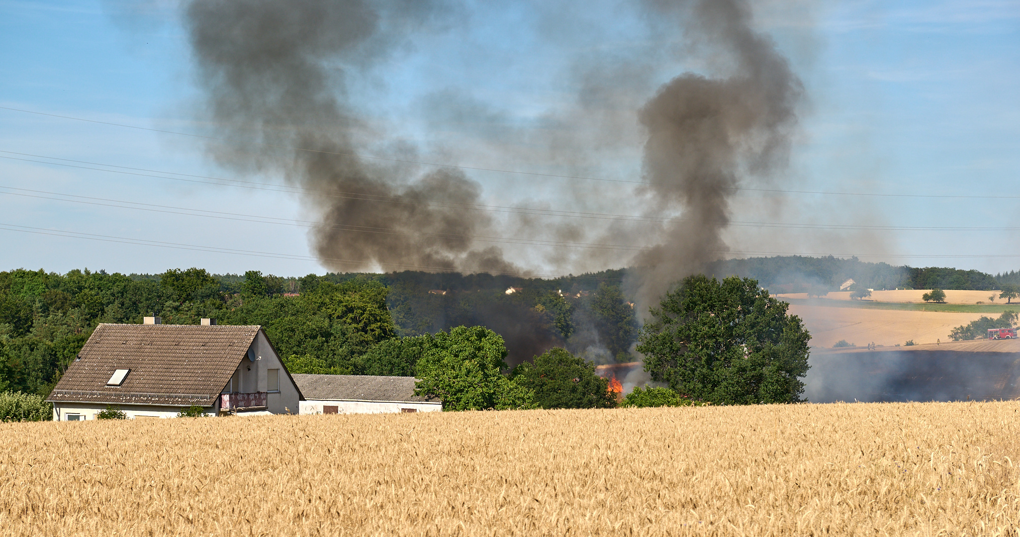 Brennender Mähdrescher verursacht Brand auf abgeerntetem Getreidefeld.