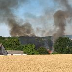 Brennender Mähdrescher verursacht Brand auf abgeerntetem Getreidefeld.