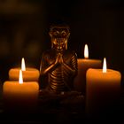 Buddha mit gefalteten Händen im Kerzenschein