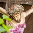 Christus am Wegkreuz mit blühendem Flieder im Vordergrund