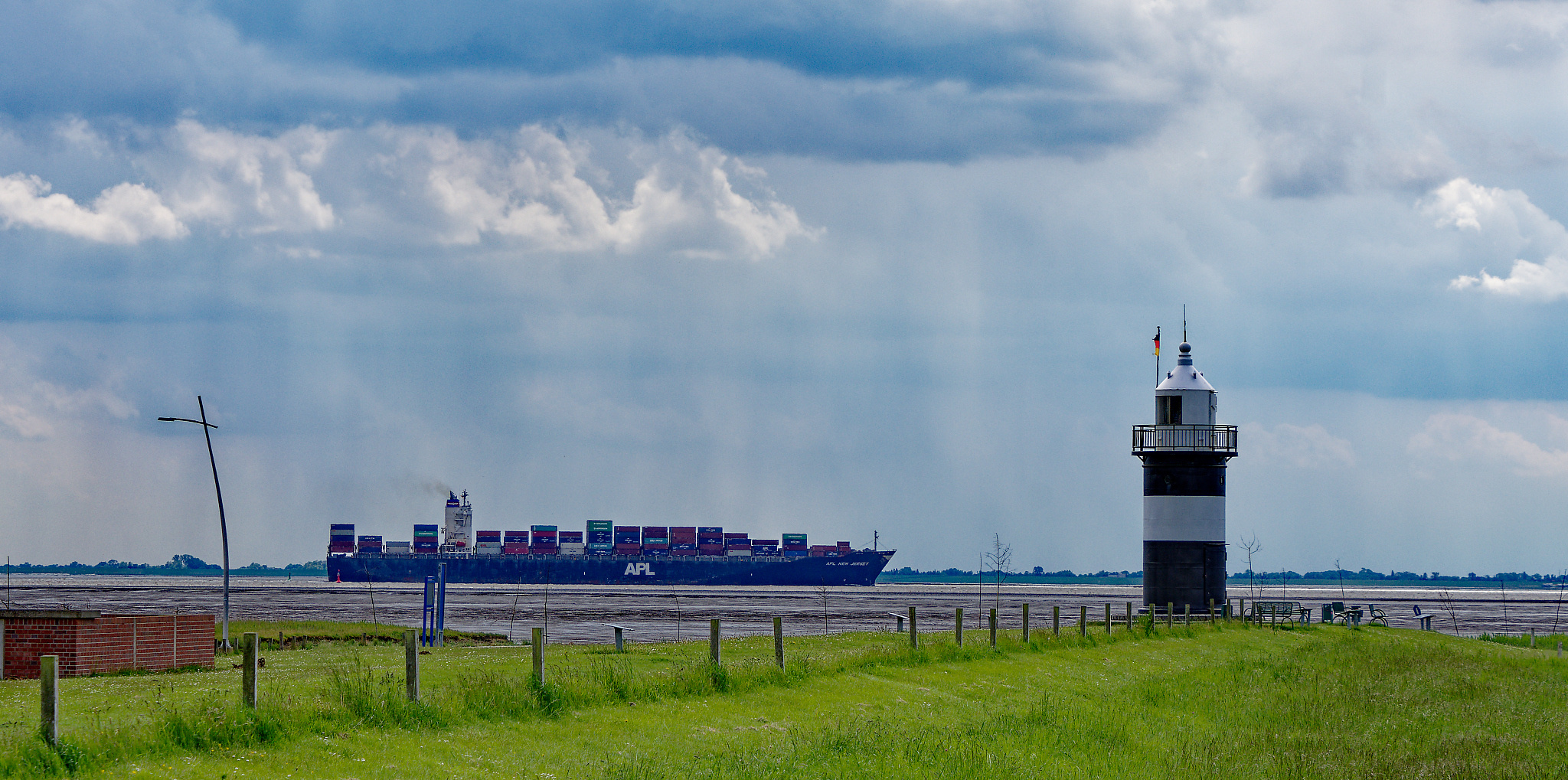Containerschiff mit Leuchtturm "Kleiner Preuße" in Wremen im Vordergrund.