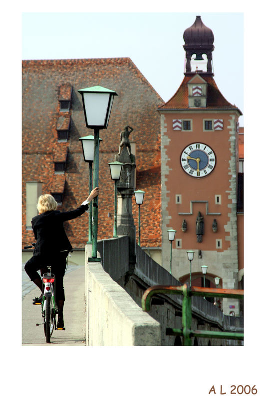 Dame auf Fahrrad lehnt sich auf der steinernen Brücke in Regensburg an einem Laternmasten an