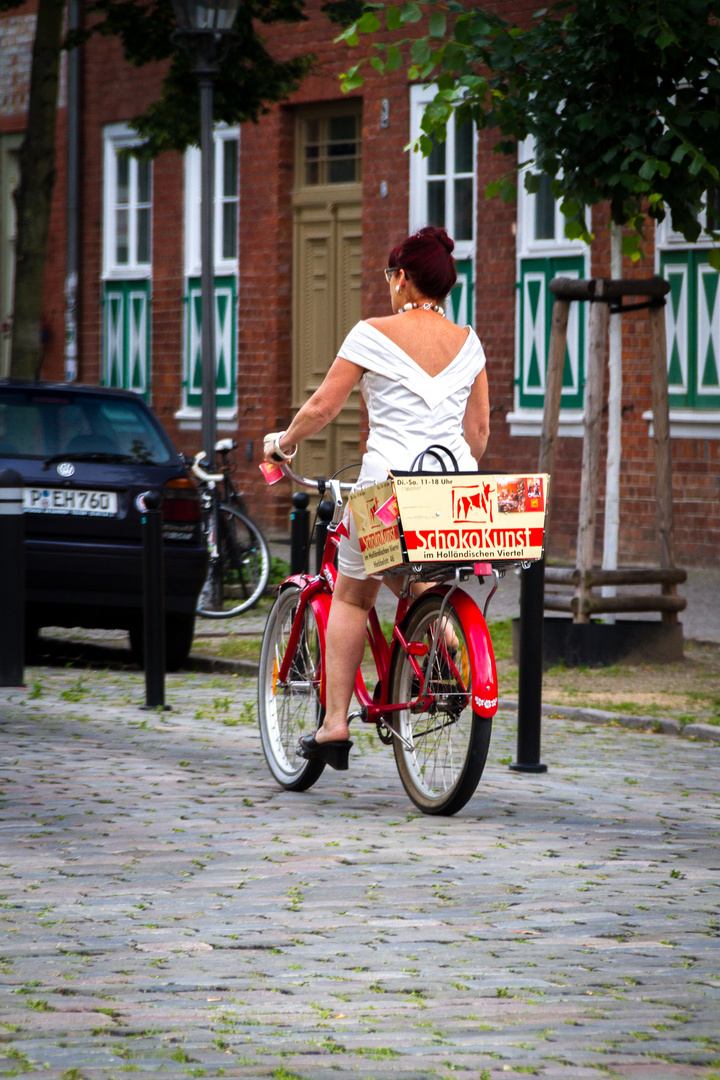 Dame in weißem Kleid auf rotem Fahrrad