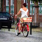 Dame in weißem Kleid auf rotem Fahrrad