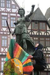 Demo Krise Frankfurt - Mann bringt Fahne an der Brunnenfigur an