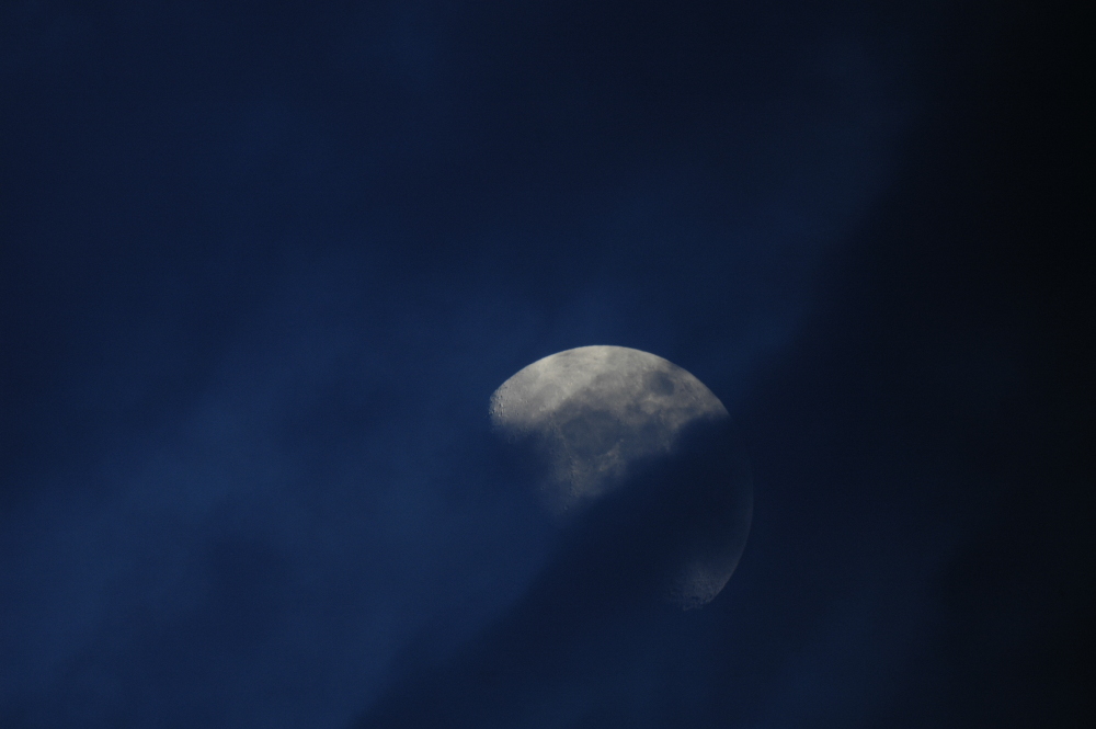 Der Mond hinter diagonal durchs Bild laufende Wolken und dem tiefblauen Abendhimmel