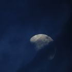Der Mond hinter diagonal durchs Bild laufende Wolken und dem tiefblauen Abendhimmel
