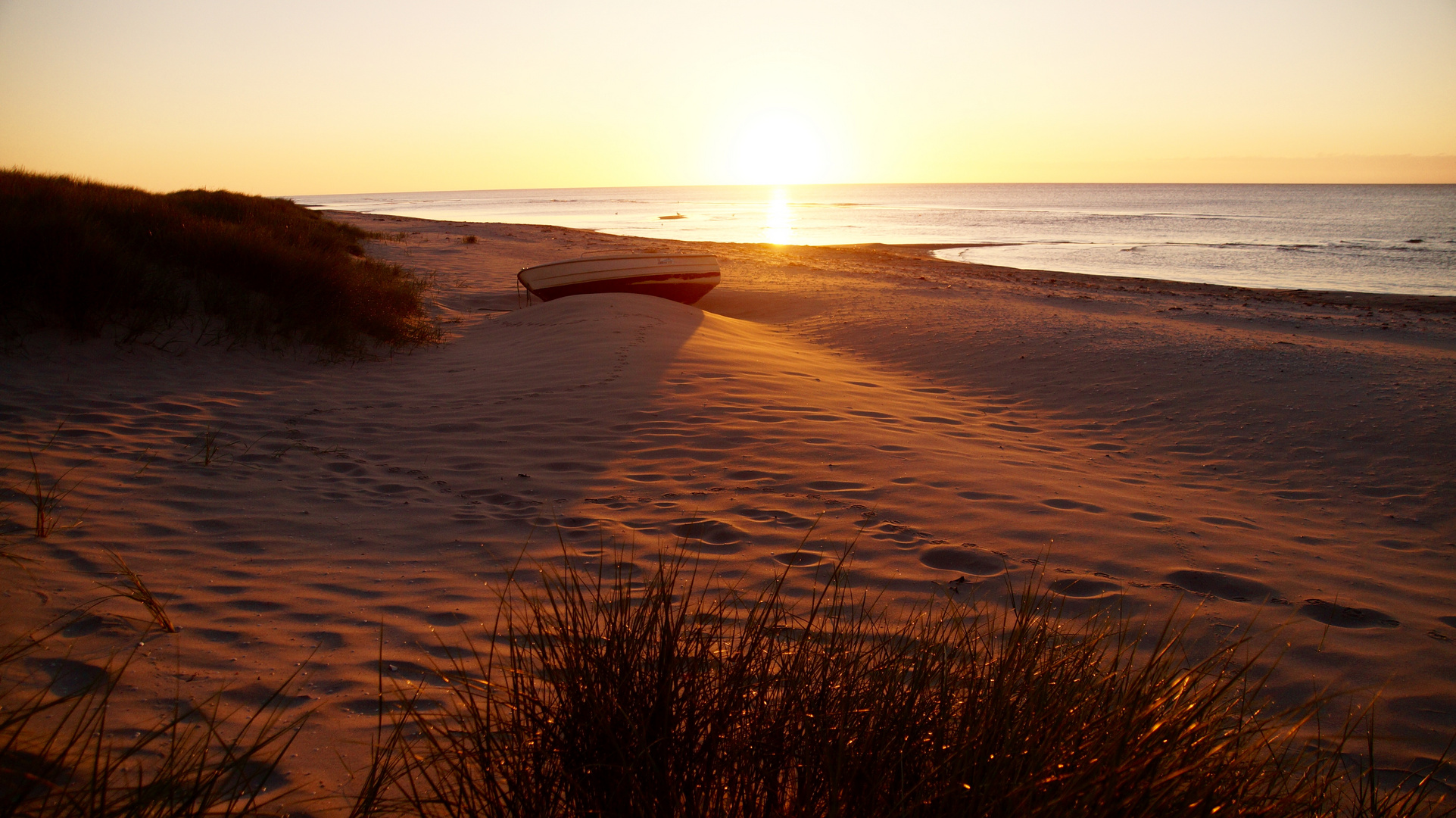 die ersten warmen morgendlichen Sonnenstrahlen legen sich über den ausgekühlten Strand