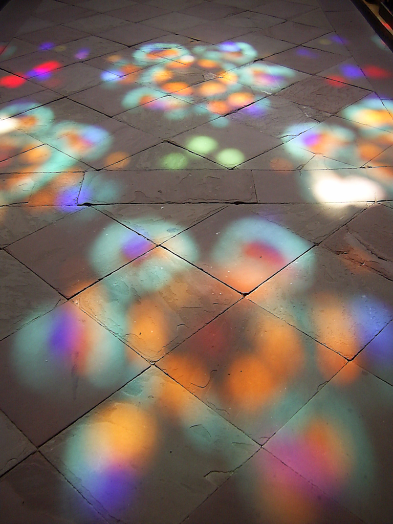 Durch das Fenster einer Kirche fällt das Licht in bunter Farbe auf den Boden