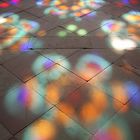 Durch das Fenster einer Kirche fällt das Licht in bunter Farbe auf den Boden