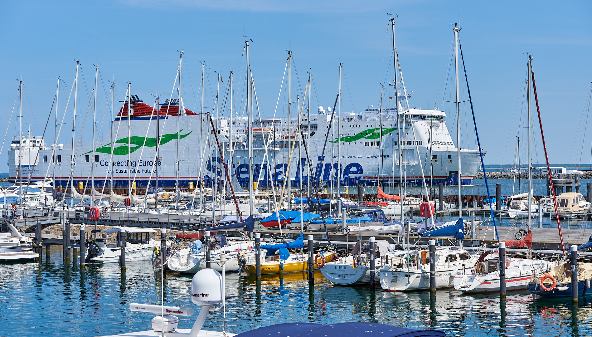 Durch die Segelmasten auf das Fährschiff geblickt wie es in den Hafen von Warnemünde fährt,…