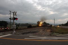 Ein Güterzug mit Getreidewagen nähert sich dem Bahnübergang mit Horn und Warnlichtern,USA