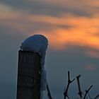 Ein Holzstecken überdeckt mit schnee und einem schönen Sonnenuntergang