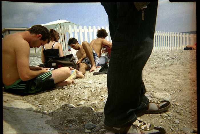 ein mensch steht mit langen hosen auf einem strand, wo andere in kurzen hosen rumlungern