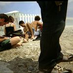 ein mensch steht mit langen hosen auf einem strand, wo andere in kurzen hosen rumlungern