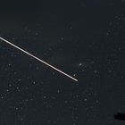 ein Satelit auf seiner Umlaufbahn mit Andromeda im Hintergrund