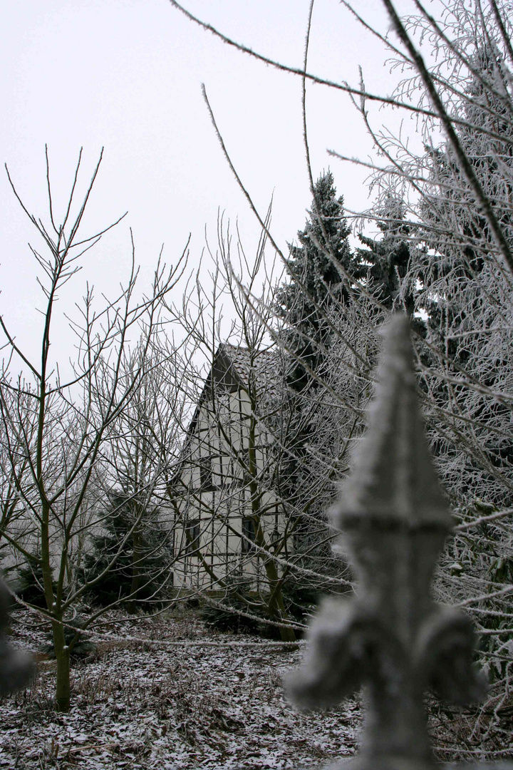 ein verschneites Bauernhaus hinterm hohen Zaun