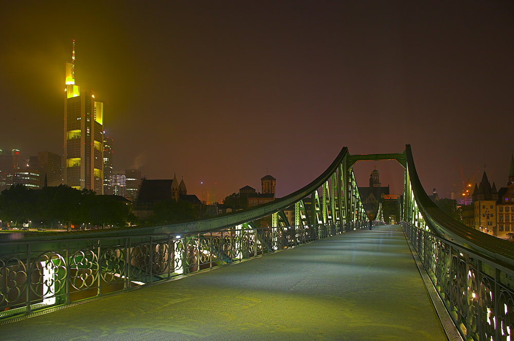Eine Brücke in Frankfurt und der Commerzbank-Tower bei Nacht.