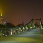 Eine Brücke in Frankfurt und der Commerzbank-Tower bei Nacht.