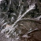 Eisblumen auf schmutziger Autoscheibe im Dunkeln mit Armatur-Reflexionen.