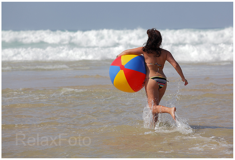 "Endlich Urlaub" - Junge Frau mit buntem Wasserball läuft Meereswellen entgegen