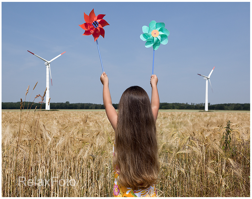 "Energiewende" - Kleines langhaariges Mädchen mit Windspiel vor Windrädern