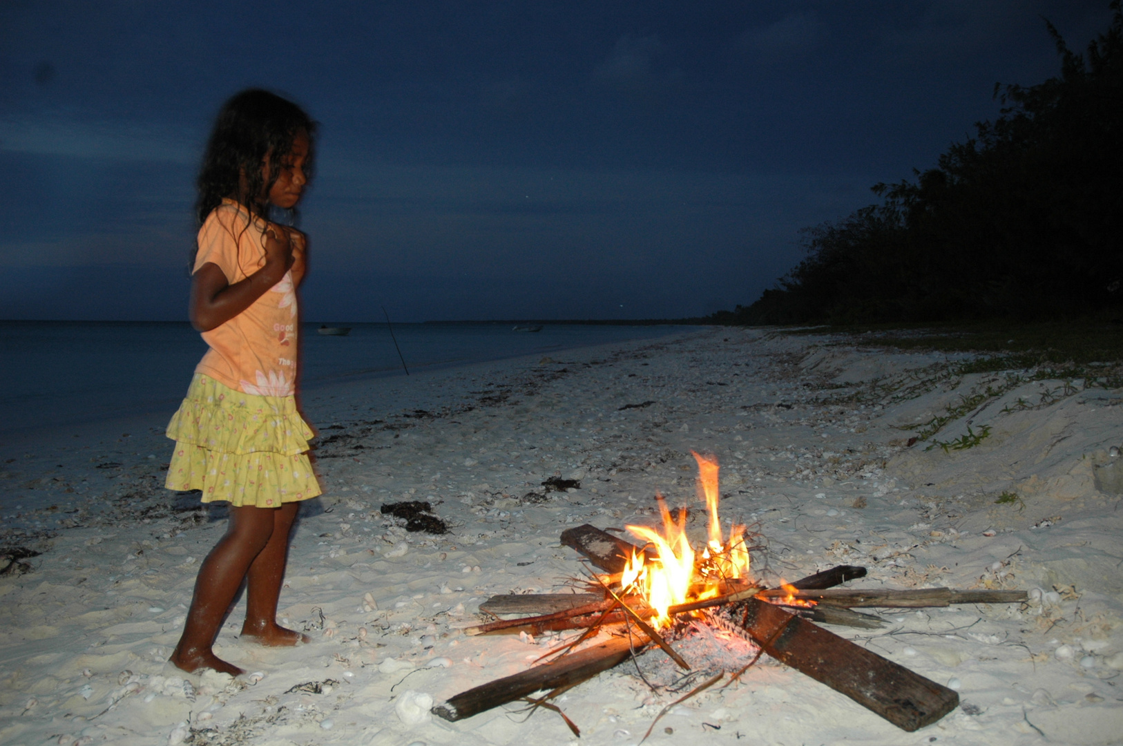 Enfant se réchauffant près d'un feu sur la plage