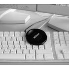 (fc-Büro 18.01.2006) Nikon-Deckel an Apple-Tastatur im Monitor-Sud, serviert auf Schreibtisch