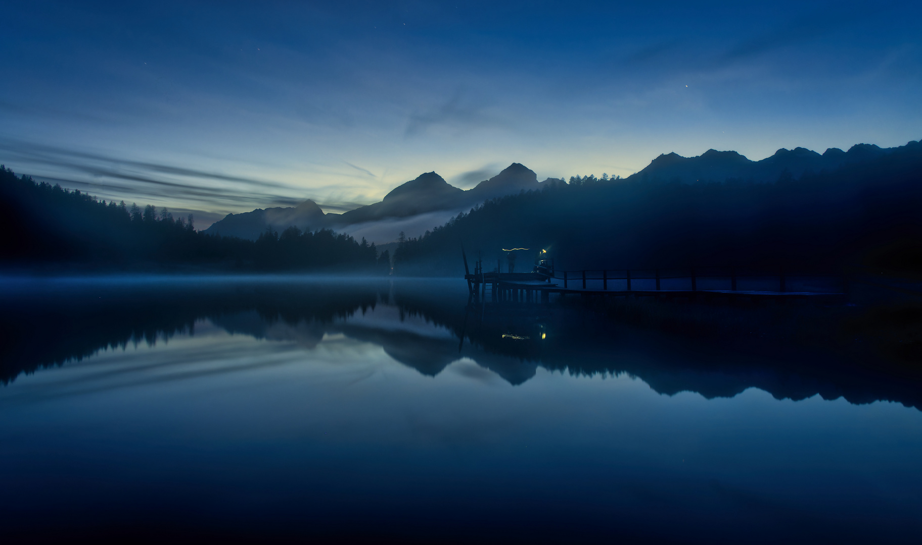 Fischer auf dem Bootssteg am Bergsee in der blauen Stunde