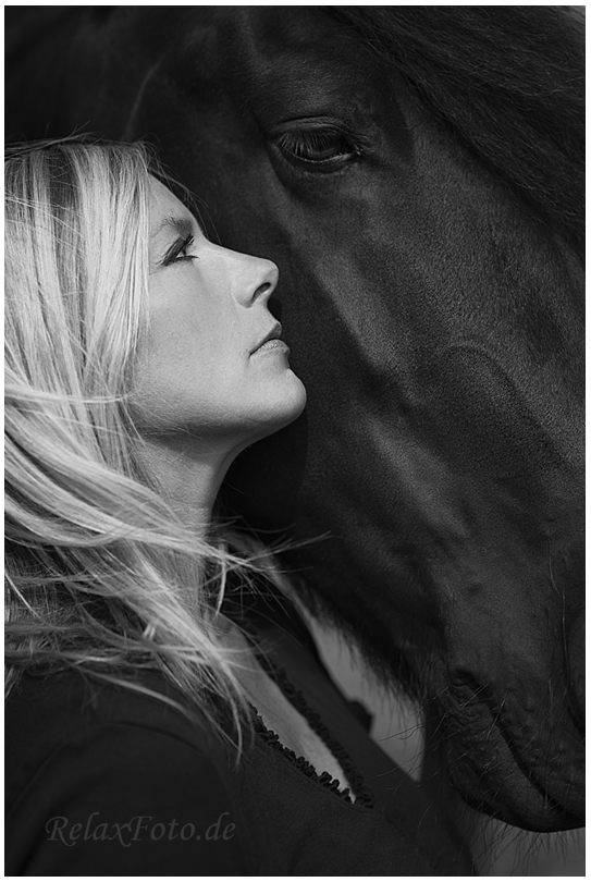 "Freundschaft zwischen Mensch und Tier" - Porträt einer blonden Frau vor schwarzem Pferdekopf