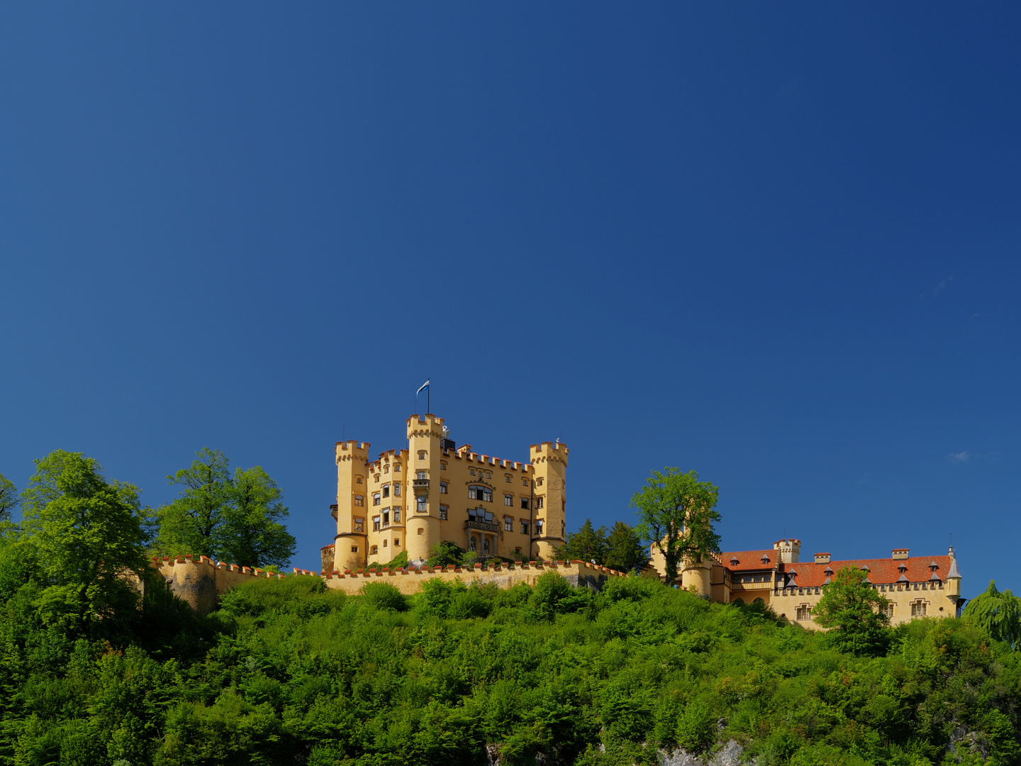 Gelbe Burg auf grünem Berg vor blauem Himmel