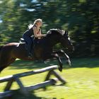 Girl With Golden Hair Rides Black Beauty Over Bar While Photographer Is Moving His Camera