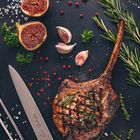 Grilled pork chop tomahawk on slate board with figs and herbs