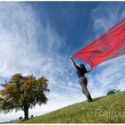 "Herbstwind" - Junge Frau mit wehendem rotem Tuch vor blauem Himmel